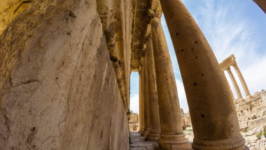 Mavi gökyüzünün altındaki antik taş sütunlar ve kalıntılar, tarihi mimariyi gözler önüne seriyor. Baalbek, Lübnan.