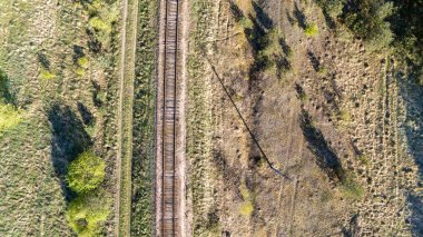 Dağınık ağaçlarla dolu çimenli bir arazide ilerleyen bir demiryolu hattının havadan görüntüsü..