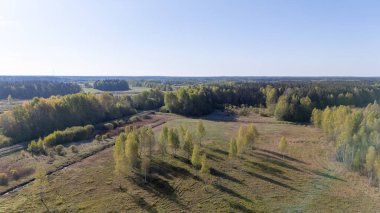 Açık tarlaları ve açık mavi gökyüzünün altındaki dağınık ağaçlarla sakin bir kırsal alanın havadan görünüşü.