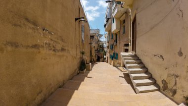 Dar sokakları taş merdivenlerle ve mavi gökyüzünün altındaki yıpranmış binalarla doldur. Lübnan, Trablus.