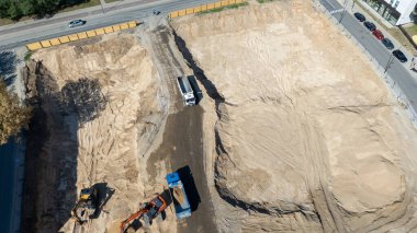 Kazı makineleri ve kamyonları olan bir inşaat alanının havadan görüntüsü.