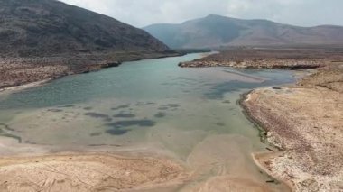 Arkasında dağlar olan kayalık bir arazide akan sakin bir nehir. Sokotra, Yemen