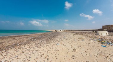 Dağınık enkaz ve açık mavi gökyüzü ile ıssız bir sahil..