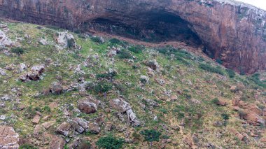 Kayalık yamaçta geniş bir mağara açığı var, seyrek bitki örtüsüyle kaplı. Sokotra, Yemen.