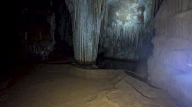 Kaba kaya duvarları, sarkıt oluşumları olan loş ışıklı mağara ve ürkütücü bir yeraltı atmosferi yaratan çatlak taş tabanı. Hoq mağarası, Sokotra.