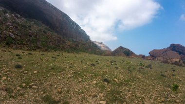 Uçsuz bucaksız dağların altındaki kayalık çimenli vadi mavi gökyüzü ve bulutlar, engebeli yaban hayatı yürüyüş ve seyahat için..