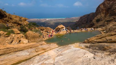 Kıyı şeridine bakan manzaralı dağ havuzu, turistler mavi gökyüzünün altında güneşli doğal çıkıntılarda yüzüyor ve dinleniyorlar..