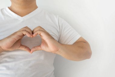 Beyaz gömlekli adam parmaklarını göğsünde kalp şeklinde birleştirdi. Sevgi ve cazibeyi beyaz bir arka planda göster