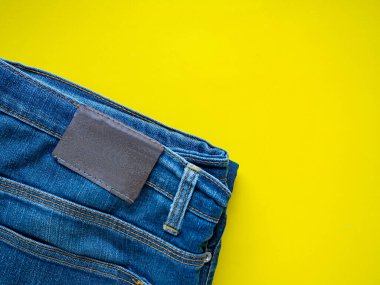 Mavi pantolon düzgünce katlanmış. Kumaşın detaylarına bakın. Sarı bir arka plan koyun.