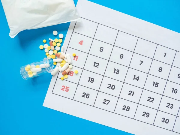 Unopened wrap of sanitary napkins With date calendar And medicine to relieve abdominal pain On a blue background