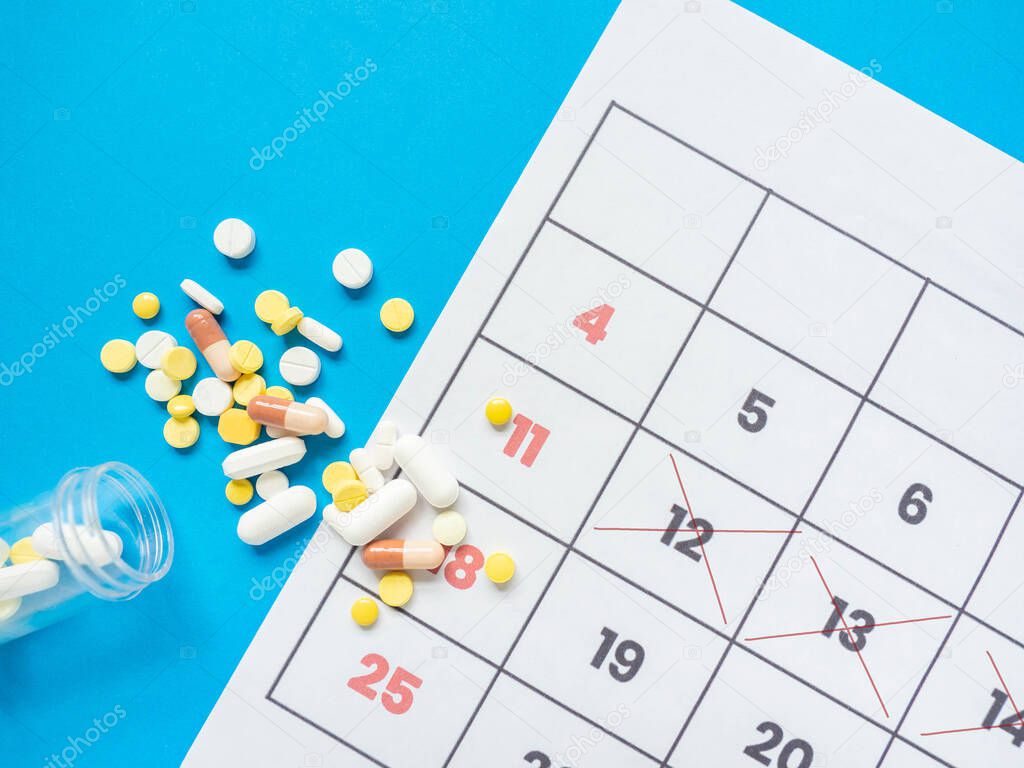 The medicinal tablets were poured out of the bottle. Placed next to a calendar to tell the time Put on a blue background.