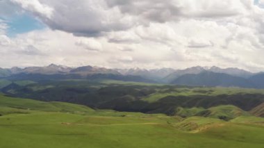 Dağ zirveleri ve çayırlar beyaz bulutların altında..