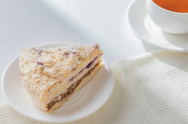 Bir parça nefis Napolyon keki, beyaz tabakta ekşi kiraz ve bir fincan çay. Ahşap masanın üzerine direk güneş ışığı ışınları. Kahvaltı konsepti.