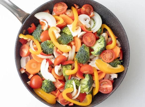 Tavada taze kesilmiş sebzeler ve beyaz arka plan. Dilimlenmiş sarı biber, mantar, vişneli domates, brokoli ve soğan pişirmeye hazır. Üst görünüm.