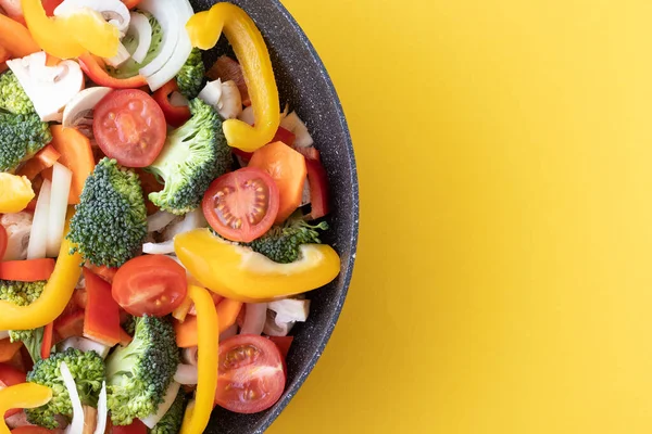 Taze kesilmiş sebzeler tavada ve sarı arka planda fotokopi alanı sağda. Dilimlenmiş sarı biber, mantar, vişneli domates, brokoli ve soğan pişirmeye hazır..