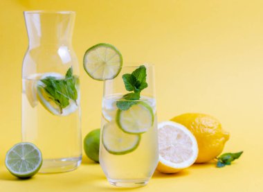 Limon dilimli bir bardak taze su ve sarı zemin üzerindeki nane artığı zehirlenmeye karşı hazırlandı..