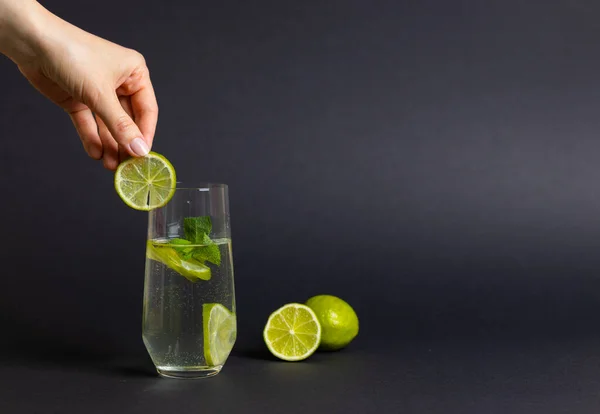 Bir bardak taze limon dilimli detoks suyu ve siyah arka planda nane şekeri. Kadın el yapımı kokteyl. Detoksifikasyon kavramı.