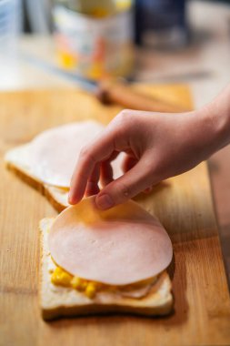 Bir insanın eli jambonu hardallı ekmeğe yerleştirir ve tahta tahtada hızlı bir sandviç yapar. Yemek hazırlama, yemek tarifleri ve ev yemeği temaları için mükemmel..