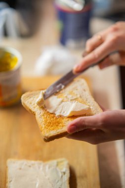 Bir insanın elleri kızarmış ekmeğe yumuşak tereyağı sürerek ev yapımı kahvaltıyı ön plana çıkarıyor. Yemek blogları veya sağlıklı beslenme kavramları için mükemmel..