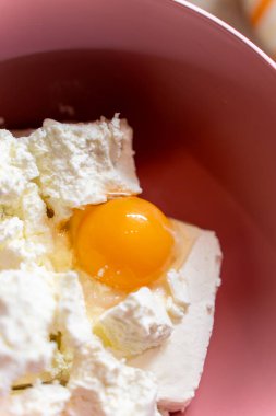 Taze çiğ yumurta sarısı canlı pembe bir kasede kremalı beyaz peynirin arasında duruyor. Pişirme, pişirme ve sağlıklı tarif içeriği için ideal.