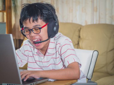 Kulaklık takan çocuk internette sohbet eden Skype öğretmeniyle masada oturuyor sınava hazırlanıyor ve ödevi için dizüstü bilgisayar kullanıyor ve online eğitim için E-öğrenim görüyor. çocuk konsepti öğrenmek.