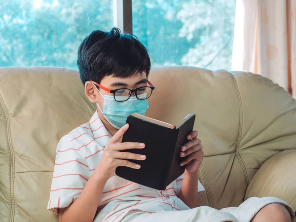 Μικρό Άρρωστο Αγόρι Διαβάζει Βιβλίο Στον Καναπέ Ενώ Φοράει Μάσκα — Φωτογραφία Αρχείου