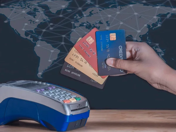Young business showing all credit cards on mobile card reader and hand entering security pin in credit card machine on world map and network datalink background. Buy, sell products and service concept