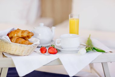 Oteldeki yatağın üzerine ahşap bir kahvaltı masası oturur. Portakal suyu, çilek, kruvasan.