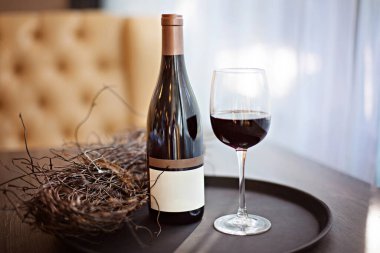 Bir şişe kırmızı şarap ve masanın üstündeki tepside dolu bir bardak.. 