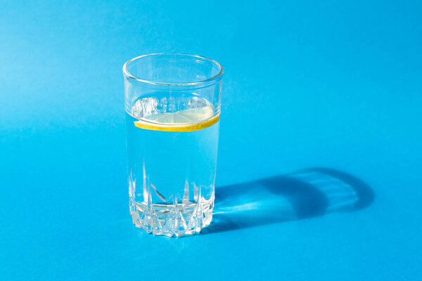 Fresh clean water in a glass with a slice of lemon on a blue background