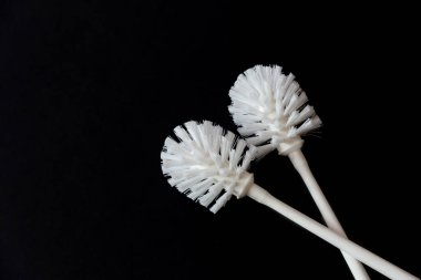 A pair of white toilet brushes on a black background. Copy space.
