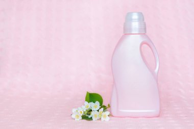 Üzerinde çamaşır deterjanı olan pembe plastik şişe yumuşak pembe arka planda yasemin çiçekleri var..