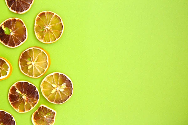 Tasty slices of dried lemon on light green background, space for text, decorative fruits frame. Flat lay. Christmas background