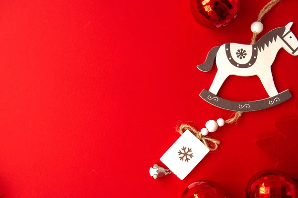 Çok renkli kırmızı Noel topları, gümüş çan ve parlak kırmızı arka planda bir at şeklinde Noel ağacı süslemesi. Tatil rutini