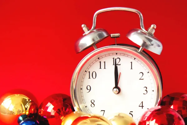 Beautiful vintage silver alarm clock and set of red, blue and golden Christmas balls on a bright red background. Time concept. Close up. Side view
