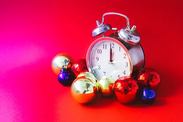 Beautiful vintage silver alarm clock and set of red, blue and golden Christmas balls on a bright red background. Time concept. Holiday routine. Side view