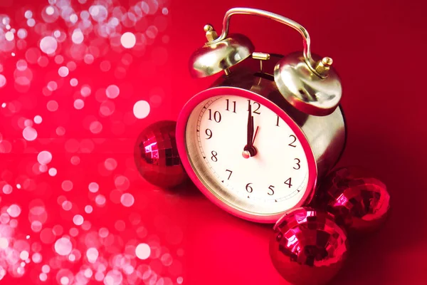 Beautiful vintage silver alarm clock and red Christmas balls on a bright red background with blur. Time concept. Holiday routine. Waiting for the holiday