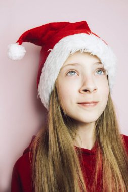 Gülümseyen, uzun saçlı, pembe arka planda tüylü Noel Baba şapkası takan güzel bir kız..