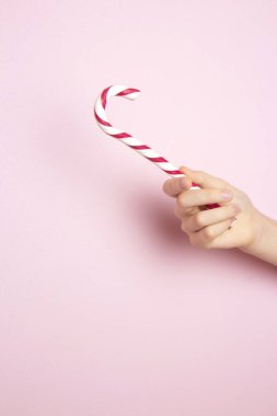 Pembe arka planda geleneksel Noel lolipopunu tutan bir kadın. Klasik parlak kırmızı ve beyaz Noel şekeri