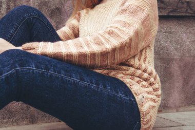 Kız kaldırımda oturuyordu. Sade bej, örgü süveter giyen güzel bir kadın dışarıda vakit geçiriyor. Kadınların yaşam tarzı.
