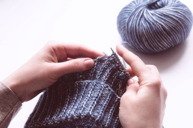 Beyaz arka planda yün mor süveter örmek için örgü iğneleri olan kadın elleri. Yünlü giysiler ören bir kadın. Tepeden. El işi kazanç konsepti