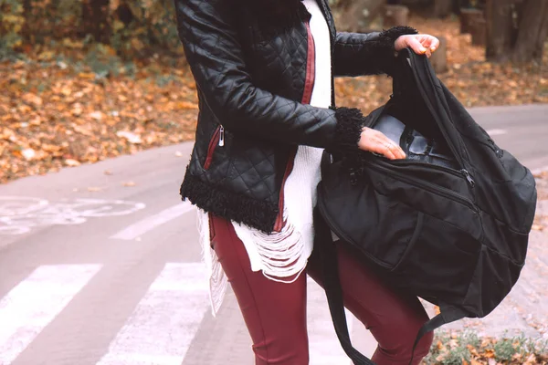 黒い革のジャケットの若い女性は 秋の森の中の自転車道の背景に黒いバックパックに物事を置きます 外の女 荷物を — ストック写真