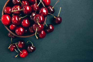 Koyu arkaplanda, ahşap bir kasede kırmızı olgun kirazların yakın çekimi. Kopyalama alanı olan yaz arkaplanı