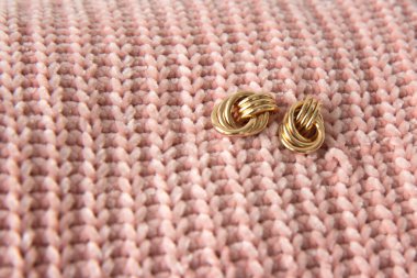 Örgü kumaşın güzel dokusunda iki güzel altın küpe. Arka plan olarak çıplak pembe kumaş ördüm. Boşluğu kopyala