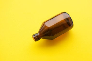 Açık sarı arka planda boş kahverengi ilaç şişesi kozmetik sıvısı. Organik, sıfır atık kozmetik kavramı