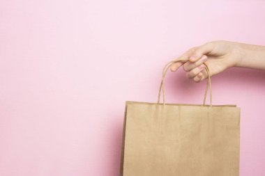 Pembe arka planda alışveriş yapmak için elinde bej bir kağıt torba tutan bir kız. Alışveriş konsepti