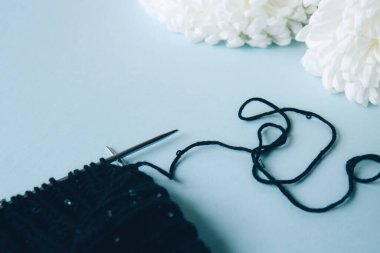 Çözülmemiş iplik. Siyah iplik, iplik yumağı, örgü iğneleri ve mavi arka planda beyaz çiçek şakayıkları. Yünlü kıyafetler örüyorum.