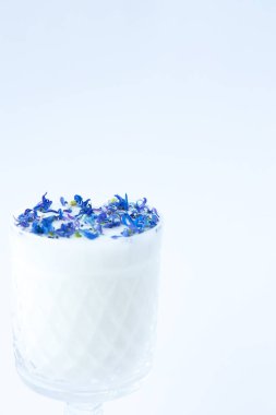 Beyaz arka planda süt ve mavi çiçek yaprakları olan güzel kristal bardaklar. Soyut arkaplan. Beyaz arka planda mavi çiçek yaprakları deseni