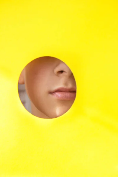 Όμορφο πρόσωπο ενός κοριτσιού που κρυφοκοιτάζει από την τρύπα σε κίτρινο χαρτί — Φωτογραφία Αρχείου