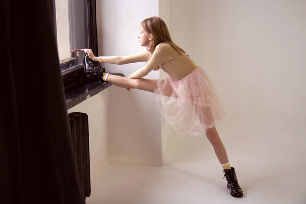 Teenage girl in a bodysuit and a fluffy tulle pink skirt looks out the window